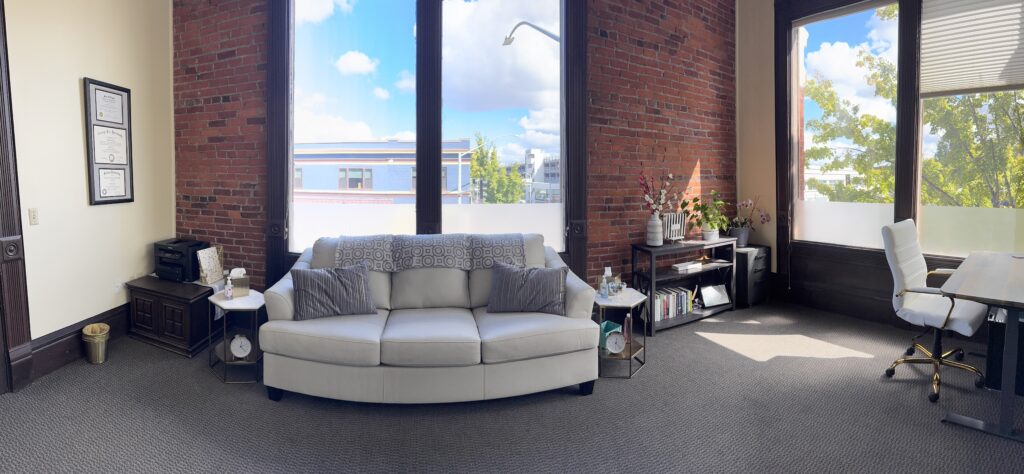 Cozy white couch with gray blanket and pillows, brick wall, plants and windows in a therapy office space